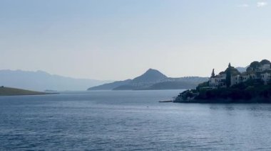 Mavi kıyı suları, Türkiye 'nin Bodrum kenti yakınlarındaki uzak dağlarla yarımadalar arasında uzanır ve sağ tarafta sakin bir sahil köyü bulunur.