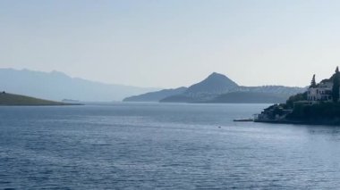 Türkiye 'nin Bodrum kenti yakınlarındaki mavi deniz, katmanlı tepeler açık bir sabah gökyüzü altında yavaş çekim kayboluyor.