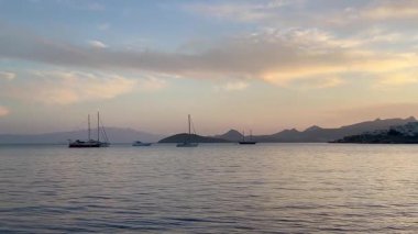 Pastel gökyüzü durgun suların üzerinde uzanıyor ve alacakaranlık yavaşça körfeze çökerken Türkiye 'nin Bodrum kenti yakınlarında demirli yelkenliler var.