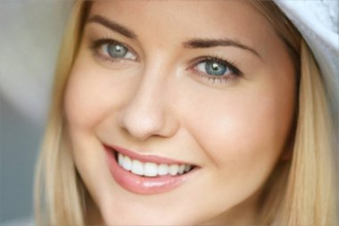 Yaz cilt bakımı ve beyaz dişler, kumsal şapkalı sarışın kadın yumuşak bir şekilde gülümsüyor, açık tenli ve açık renk makyajlı.