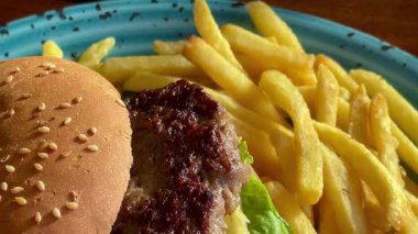 Marul, domates ve turşulu ızgara burger, deniz kenarındaki bir restoranda turkuaz bir tabakta altın cipsle servis edilir.