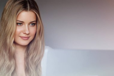 Laptop yaşam tarzı ve evden çalışma, internet kursu, bilgisayar kullanan uzun dalgalı saçlı sarışın kadın, doğal makyaj ve mavi gözler, dijital yaşam dengesi.