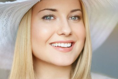 Yaz cilt bakımı ve beyaz dişler, kumsal şapkalı sarışın kadın yumuşak bir şekilde gülümsüyor, açık tenli ve açık renk makyajlı.