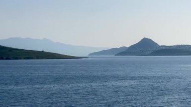 Türkiye 'nin Bodrum kenti yakınlarındaki mavi deniz, katmanlı tepeler açık bir sabah gökyüzü altında yavaş çekim kayboluyor.