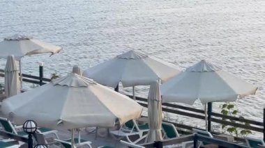 Şemsiyeler ve dinlenme yerleri, Türkiye 'nin Bodrum kenti yakınlarında sakin mavi dalgalara, yavaş çekime bakan huzurlu bir rıhtımda kuyruk oluşturuyorlar.