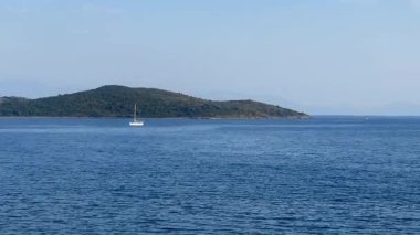 Yelkenli, Türkiye 'nin Bodrum kenti yakınlarındaki derin mavi sularda, berrak bir gökyüzünün altında sessizce dinlenen yeşil bir adayla sürüklenir.