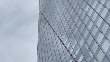 Londra 'daki Çömlek' in dramatik yükseliş manzarası, cam cephesi bulutlu gökyüzüne doğru inceliyor, modern İngiliz mimarisinin yüksekliğini ve zarafetini yakalıyor, yavaş çekim.