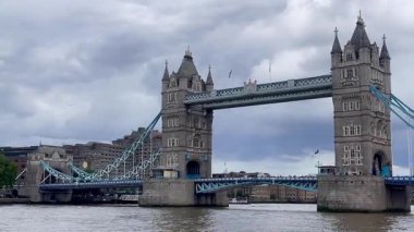 Londra 'daki Tower Bridge' in görkemli bir yakın görüntüsü, Thames Nehri 'nin üzerinde dramatik bulutların altında cesurca duruyor, değerli bir İngiliz ikonu, yavaş çekim