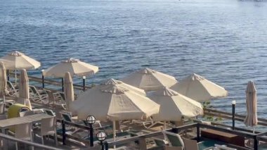 Şemsiyeler ve dinlenme yerleri, Türkiye 'nin Bodrum kenti yakınlarında sakin mavi dalgalara, yavaş çekime bakan huzurlu bir rıhtımda kuyruk oluşturuyorlar.