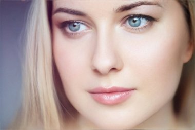 Doğal güzellik ve cilt bakımı, açık tenli sarışın kadın, yumuşak makyaj ve mavi gözler, sessiz bir arkaplanda sessizce poz veriyor.