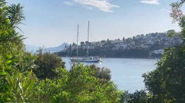 Bereketli kıyı yeşilliklerinde, Türkiye 'nin Bodrum kenti yakınlarındaki durgun mavi denizde bir yelkenli süzülüyor, tepe kenarındaki beyaz villalar ötesinde, ağır çekimde