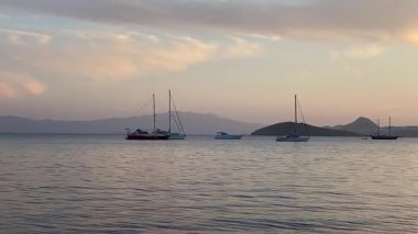 Pastel gökyüzü durgun suların üzerinde uzanıyor ve alacakaranlık yavaşça körfeze çökerken Türkiye 'nin Bodrum kenti yakınlarında demirli yelkenliler var.