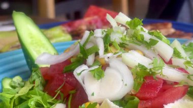 Canlı, mavi bir kasede servis edilen domates, soğan, marul ve limon dilimlerinden oluşan taze bir Akdeniz salatası..