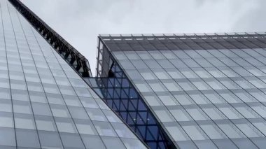 Londra 'daki Çömlek' in dramatik yükseliş manzarası, cam cephesi bulutlu gökyüzüne doğru inceliyor, modern İngiliz mimarisinin yüksekliğini ve zarafetini yakalıyor, yavaş çekim.