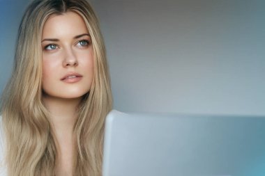 Laptop yaşam tarzı ve evden çalışma, internet kursu, bilgisayar kullanan uzun dalgalı saçlı sarışın kadın, doğal makyaj ve mavi gözler, dijital yaşam dengesi.