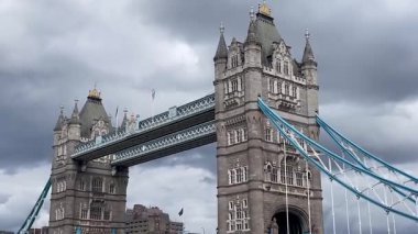 Londra 'daki Tower Bridge' in görkemli bir yakın görüntüsü, Thames Nehri 'nin üzerinde dramatik bulutların altında cesurca duruyor, değerli bir İngiliz ikonu, yavaş çekim