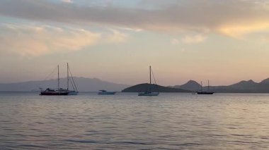 Pastel gökyüzü durgun suların üzerinde uzanıyor ve alacakaranlık yavaşça körfeze çökerken Türkiye 'nin Bodrum kenti yakınlarında demirli yelkenliler var.