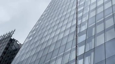 Londra 'daki Çömlek' in dramatik yükseliş manzarası, cam cephesi bulutlu gökyüzüne doğru inceliyor, modern İngiliz mimarisinin yüksekliğini ve zarafetini yakalıyor, yavaş çekim.