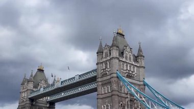 Londra 'daki Tower Bridge' in görkemli bir yakın görüntüsü, Thames Nehri 'nin üzerinde dramatik bulutların altında cesurca duruyor, değerli bir İngiliz ikonu, yavaş çekim