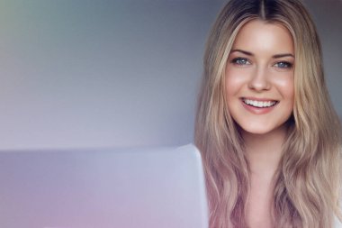 Laptop yaşam tarzı ve evden çalışma, internet kursu, bilgisayar kullanan uzun dalgalı saçlı sarışın kadın, doğal makyaj ve mavi gözler, dijital yaşam dengesi.