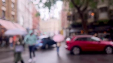 Yağmurlu bir Londra caddesinin bulanık görüntüsü, şemsiyeler, kırmızı çift katlı otobüsler, ve damlayan ağaçların altından geçen yayalar, atmosferik ve dengesiz, dağılmış
