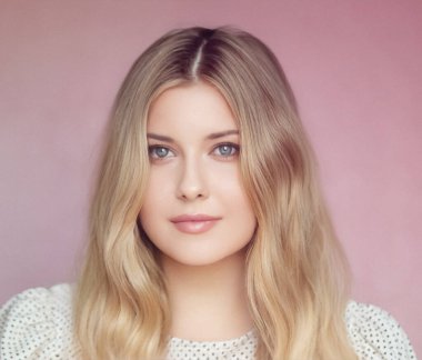 Doğal güzellik ve cilt zarafeti, yumuşak dalgalı sarışın kadın ve mavi gözler pembe arka plana karşı poz veriyor pürüzsüz makyajlı ve parlak tenli.