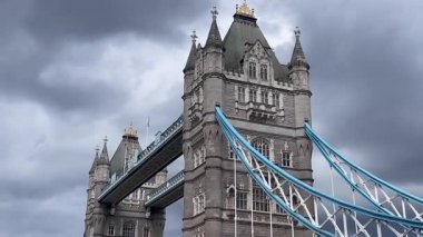Londra 'daki Tower Bridge' in görkemli bir yakın görüntüsü, Thames Nehri 'nin üzerinde dramatik bulutların altında cesurca duruyor, değerli bir İngiliz ikonu, yavaş çekim