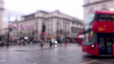 Yağmurlu bir Londra caddesinin bulanık görüntüsü, şemsiyeler, kırmızı çift katlı otobüsler, ve damlayan ağaçların altından geçen yayalar, atmosferik ve dengesiz, dağılmış
