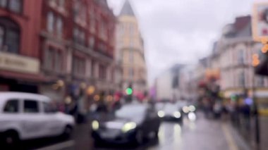 Yağmurlu bir Londra caddesinin bulanık görüntüsü, şemsiyeler, kırmızı çift katlı otobüsler, ve damlayan ağaçların altından geçen yayalar, atmosferik ve dengesiz, dağılmış