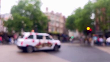 Yağmurlu bir Londra caddesinin bulanık görüntüsü, şemsiyeler, kırmızı çift katlı otobüsler, ve damlayan ağaçların altından geçen yayalar, atmosferik ve dengesiz, dağılmış