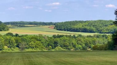 Yumuşak mavi gökyüzünün altındaki katmanlı İngiliz kırsal tepelerinin ve ağaçların geniş bir görüntüsü, yaz ışığı altında, yavaş çekimde.