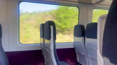 Boş tren koltukları geniş pencerelere bakıyor. Manzaralı İngiliz kırsal manzarası ve dışarıda yeşil alanlar var. Yavaş çekim.