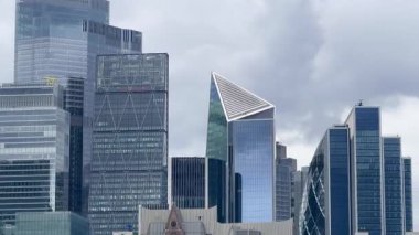 Londra 'nın merkezindeki modern yüksek binalarda dramatik gri gökyüzü altında cam ve çelik mimari, yavaş çekim