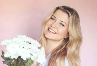 Beyaz kasımpatı tutan, gülümseyen kadın, pastel pembe bir duvara karşı poz veriyor, ışık saçan sıcak yürekli bir İngiliz sıcaklığı ve genç İngiliz cazibesi