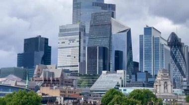 Londra 'nın merkezindeki modern yüksek binalarda dramatik gri gökyüzü altında cam ve çelik mimari, yavaş çekim
