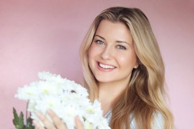 Beyaz kasımpatı tutan, gülümseyen kadın, pastel pembe bir duvara karşı poz veriyor, ışık saçan sıcak yürekli bir İngiliz sıcaklığı ve genç İngiliz cazibesi