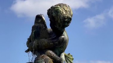 Mavi İngiliz yaz gökyüzünün altında yumuşak suların aktığı bir balığı kucaklayan melek çeşme heykeli, resmi arka plan, yavaş çekim