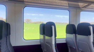 Boş tren koltukları geniş pencerelere bakıyor. Manzaralı İngiliz kırsal manzarası ve dışarıda yeşil alanlar var. Yavaş çekim.