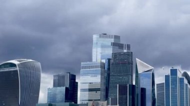 Londra 'nın merkezindeki modern yüksek binalarda dramatik gri gökyüzü altında cam ve çelik mimari, yavaş çekim