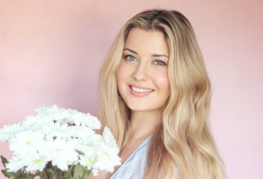 Beyaz kasımpatı tutan, gülümseyen kadın, pastel pembe bir duvara karşı poz veriyor, ışık saçan sıcak yürekli bir İngiliz sıcaklığı ve genç İngiliz cazibesi