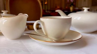 Krema sürahisi, çaydanlık ve altın çerçeveli fincanla sessiz bir çay seti geleneksel İngiliz konukseverliğinin cazibesini çağrıştırıyor, yavaş çekim.