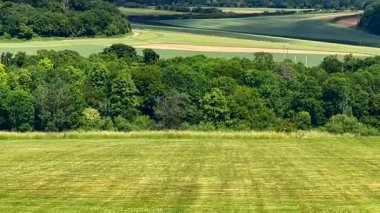 Yumuşak mavi gökyüzünün altındaki katmanlı İngiliz kırsal tepelerinin ve ağaçların geniş bir görüntüsü, yaz ışığı altında, yavaş çekimde.