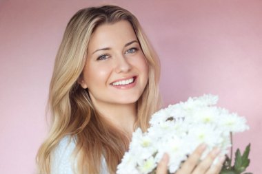 Beyaz kasımpatı tutan, gülümseyen kadın, pastel pembe bir duvara karşı poz veriyor, ışık saçan sıcak yürekli bir İngiliz sıcaklığı ve genç İngiliz cazibesi