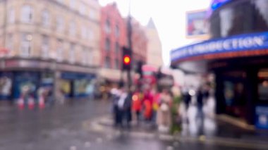 Yağmurlu bir Londra caddesinin bulanık görüntüsü, şemsiyeler, kırmızı çift katlı otobüsler, ve damlayan ağaçların altından geçen yayalar, atmosferik ve dengesiz, dağılmış