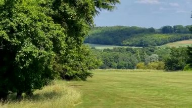 Parlak mavi gökyüzünün altında İngiliz çimenliği dağınık bulutlar ve katmanlı yemyeşil, sakin kırsal manzara, yavaş çekim
