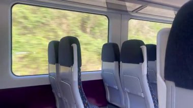 Boş tren koltukları geniş pencerelere bakıyor. Manzaralı İngiliz kırsal manzarası ve dışarıda yeşil alanlar var. Yavaş çekim.