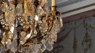 Süslü bir altın ve kristal avizeye yakın çekim, mum ampulleri ile, bir İngiliz malikanesinde el boyaması klasik bir duvara karşı, yavaş çekim