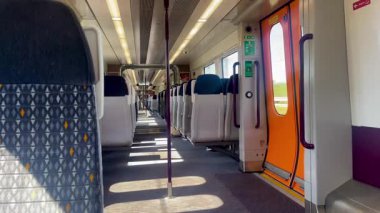 Boş tren koltukları geniş pencerelere bakıyor. Manzaralı İngiliz kırsal manzarası ve dışarıda yeşil alanlar var. Yavaş çekim.