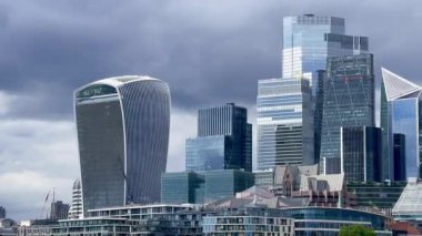 Londra 'nın merkezindeki modern yüksek binalarda dramatik gri gökyüzü altında cam ve çelik mimari, yavaş çekim