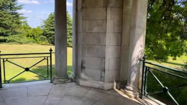 Kırpılmış yeşil çitler ve mavi İngiliz gökyüzünün altındaki altın taş yol tarafından çerçevelenmiş bahçe köşkü, geleneksel ve zamansız, yavaş çekim